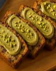 Bananenbrot Scheiben mit Pistaziencreme bestrichen und gehackten Pistazien bestreut auf Holzteller