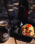 Klea Koroneiki Olivenöl in schwarzer Keramikflasche neben Pasta mit Tomaten und Kräutern angerichtet – natives Olivenöl extra Griechenland