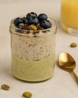 Glas mit Pistazien Overnight Oats geschichtet mit Chia Pudding, Topping aus Blaubeeren und Pistazien