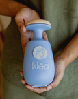 Klea natives Olivenöl extra Galani in blauer Keramikflasche mit Holzdeckel wird in beiden Händen gehalten
