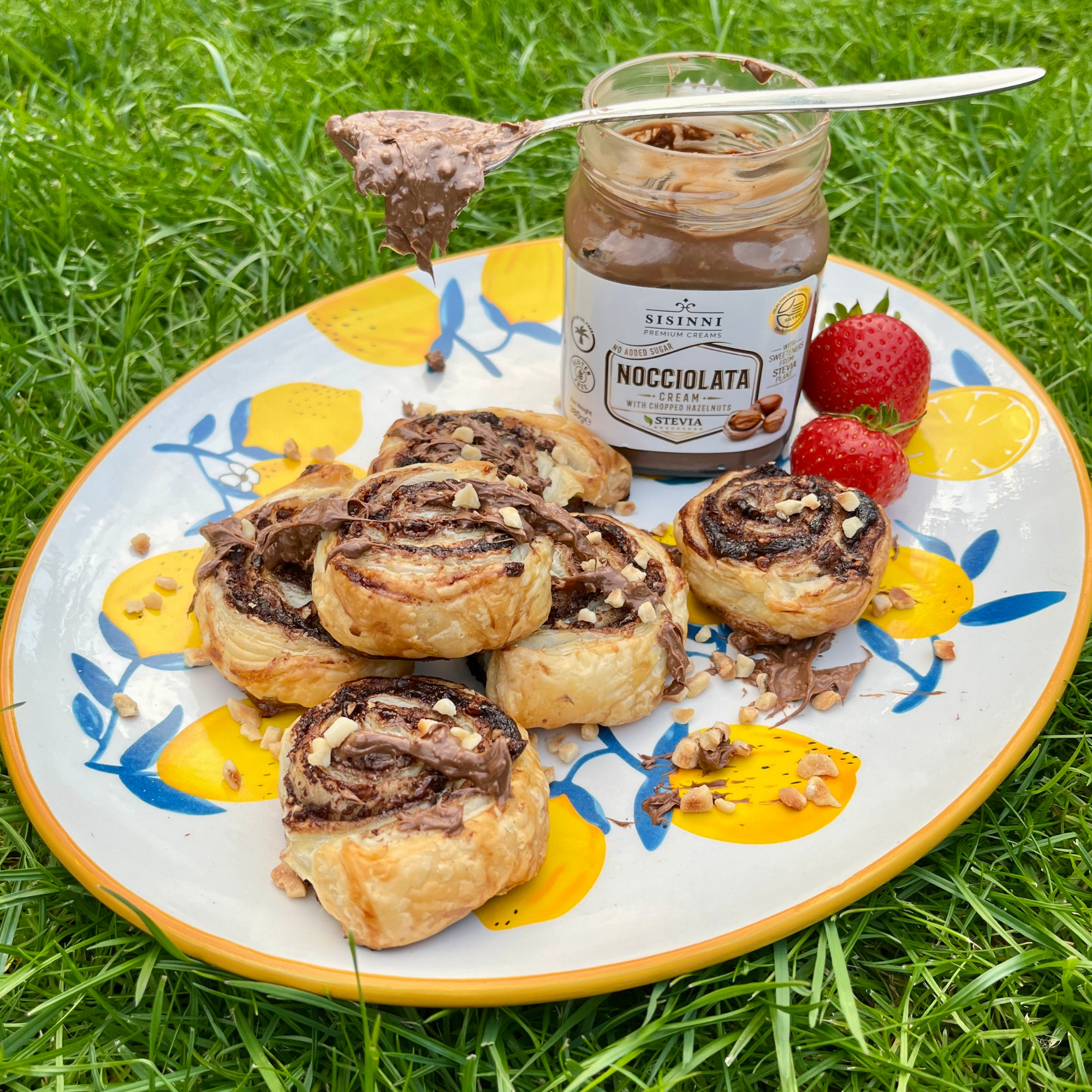 Blätterteig Schnecken mit Haselnusscreme Füllung und gehackten Haselnüssen auf Teller im Freien mit geöffnetem Glas Haselnusscreme ohne Zuckerzusatz glutenfrei und ohne Palmöl