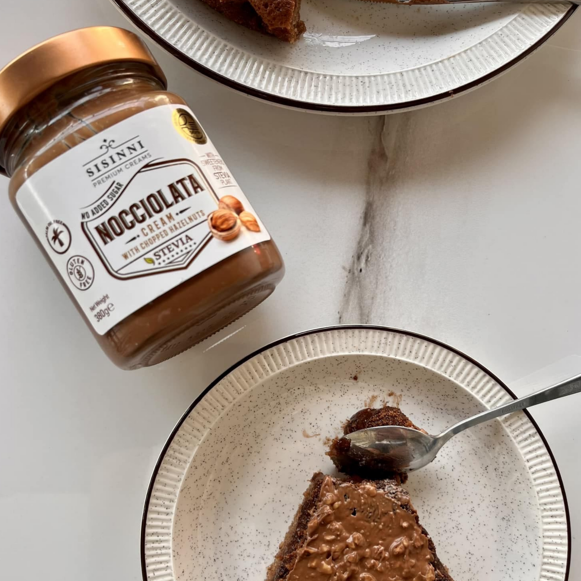 Schokoladenkuchen ohne Zuckerzusatz glutenfrei und ohne Palmöl Stück mit Haselnusscreme Topping und cremiger Haselnussfüllung auf Dessertteller mit Glas Haselnusscreme im Hintergrund