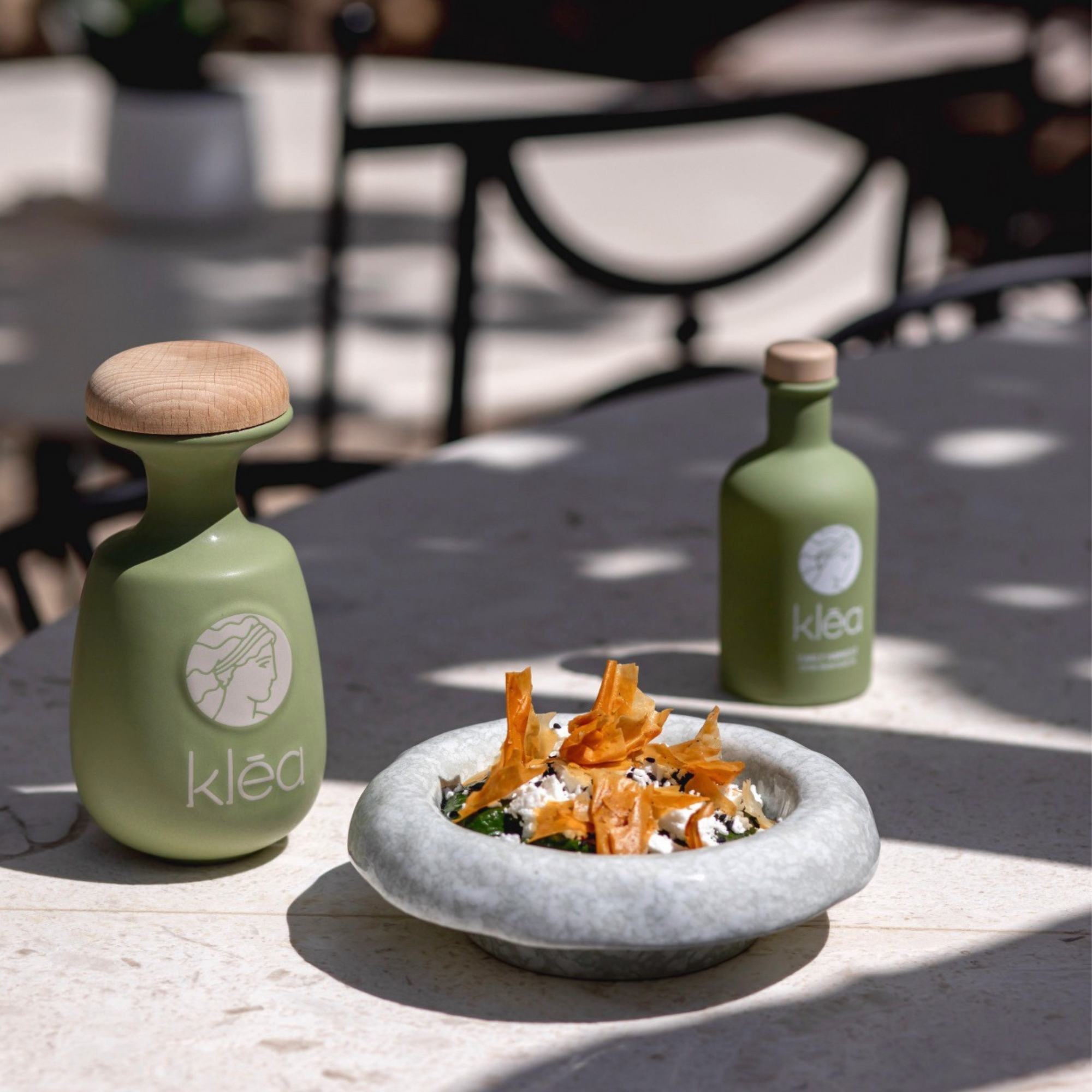 Klea Frühernte Olivenöl in grüner Keramikflasche neben mediterranem Gericht mit Feta und Gemüse – Premium Olivenöl aus Griechenland